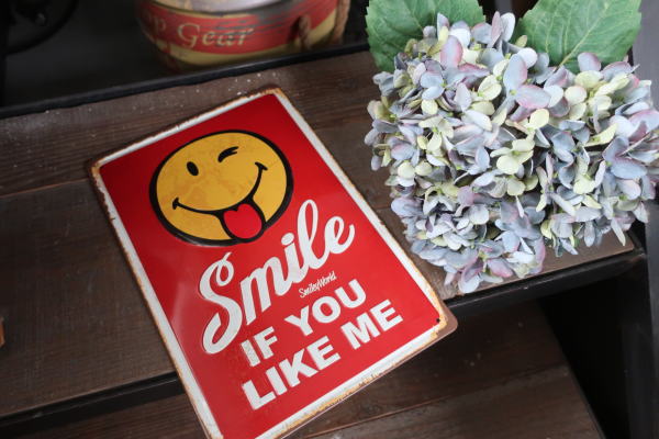 赤地にスマイルマークが描かれた縦長サインプレート